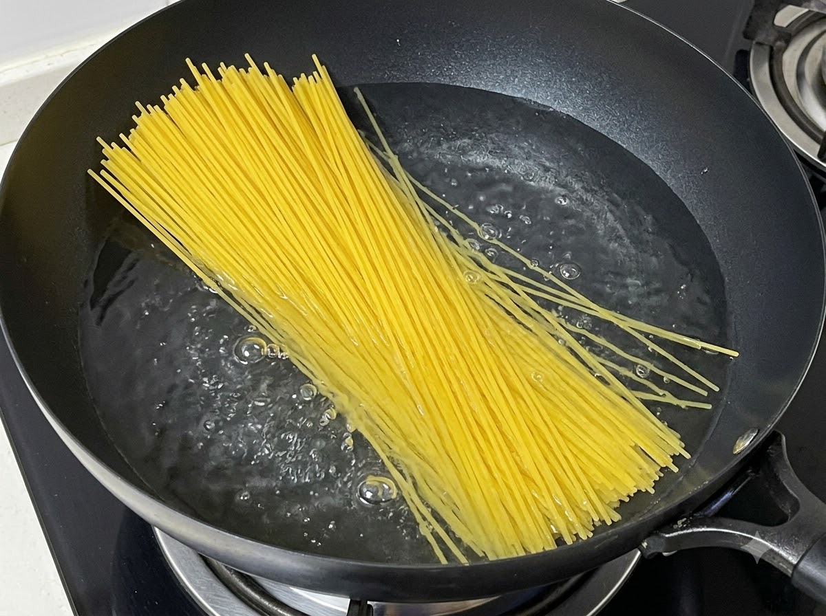 Un manojo de fideos de espagueti secos siendo sumergidos en una olla con agua hirviendo.