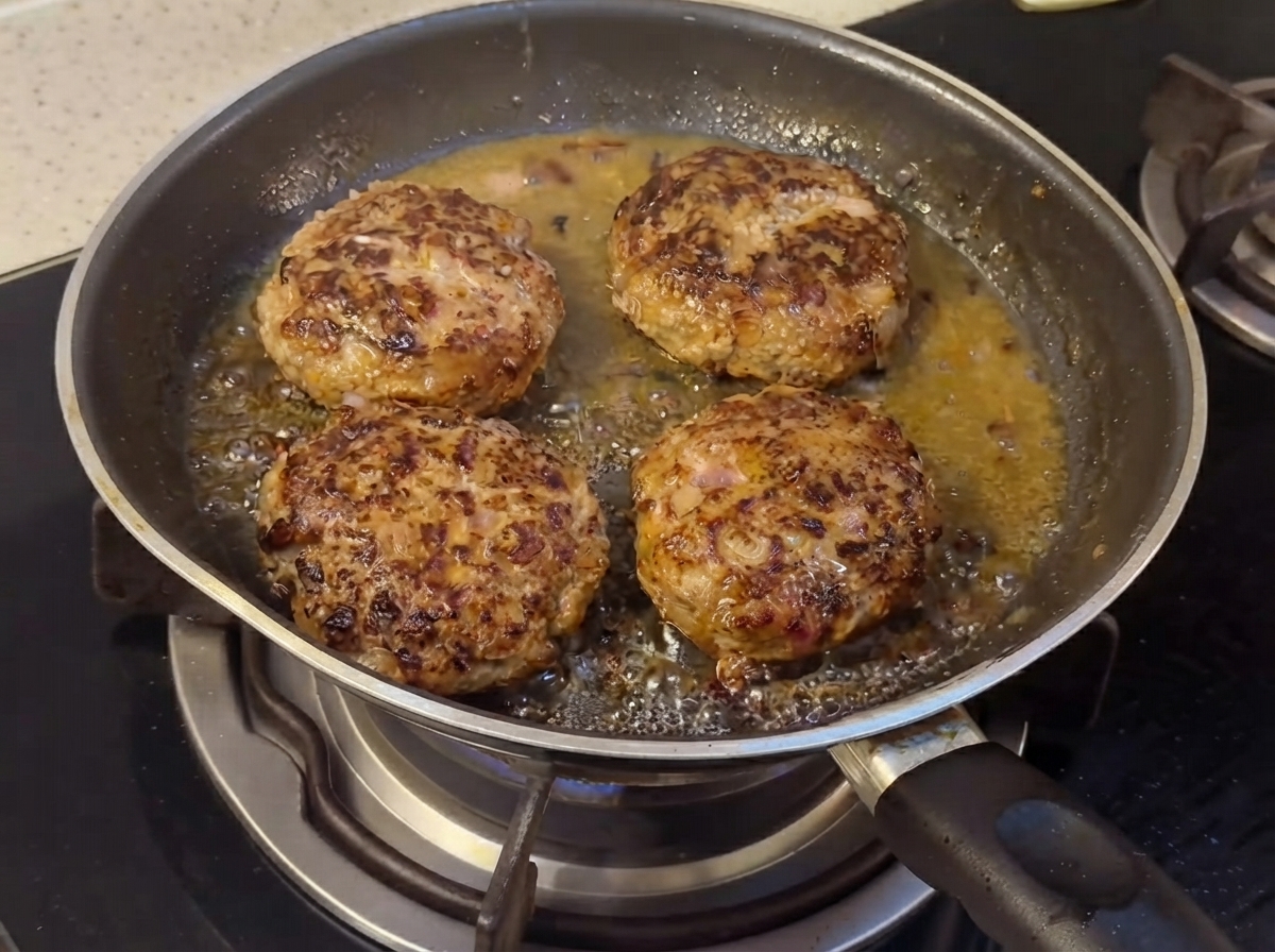 Hamburguesas cocinándose en una sartén con ingredientes líquidos de salsa comenzando a combinarse.