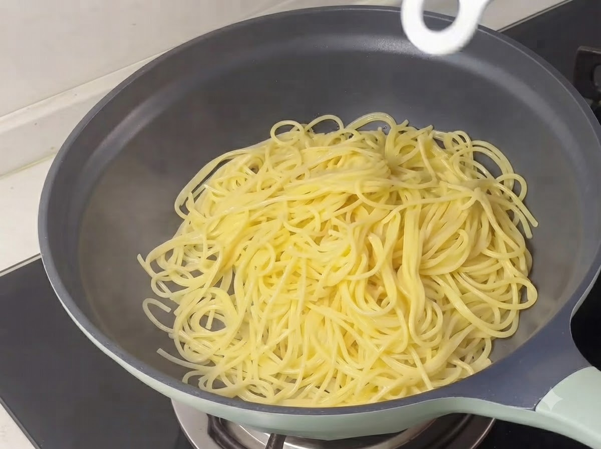 Hebras de espagueti amarillo cocido amontonadas dentro de una sartén.