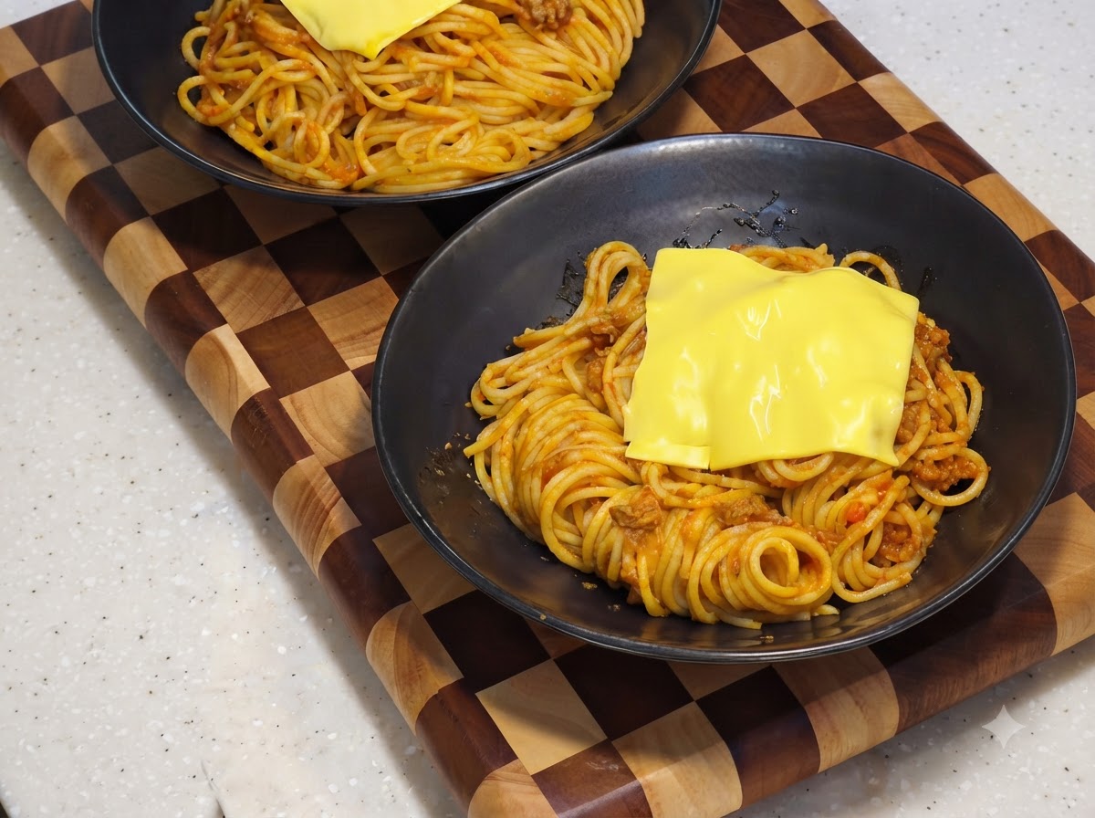 Una rodaja de queso amarillo derritiéndose sobre la base de espaguetis dentro de un tazón negro para servir.