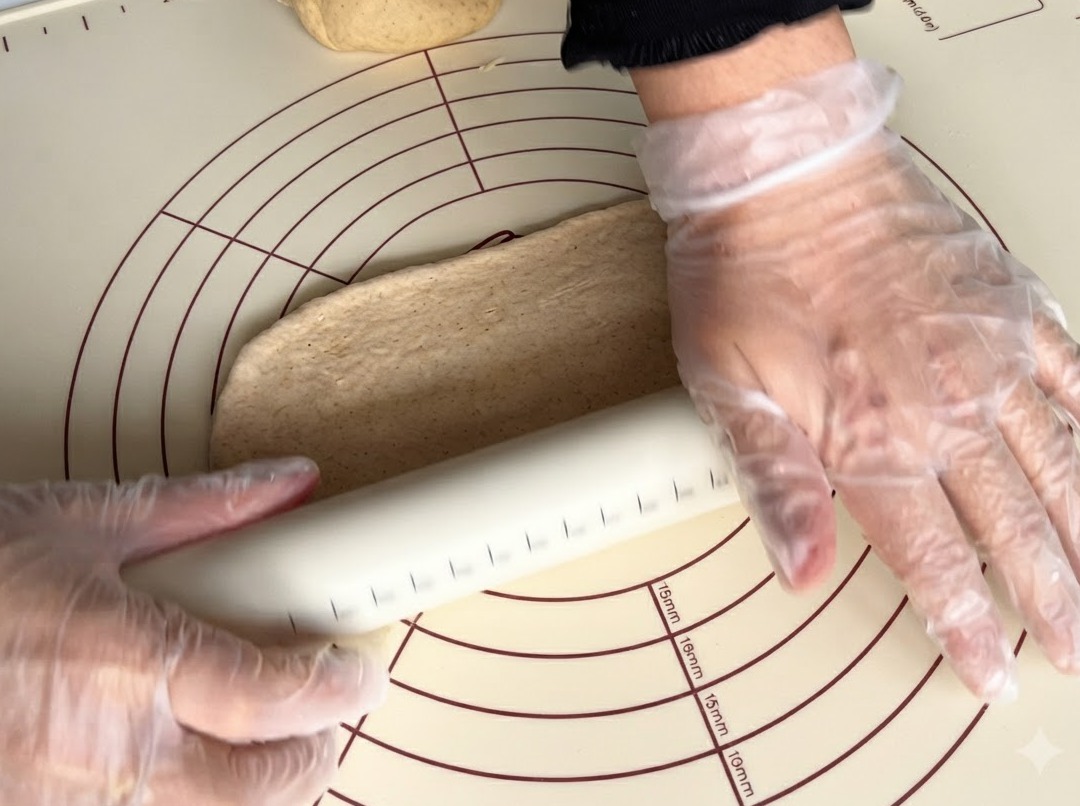 Un rodillo aplanando un trozo de masa integral sobre una alfombrilla de silicona.