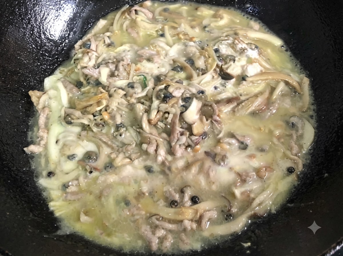 Una mezcla espesa y burbujeante siendo removida continuamente dentro de un wok negro.