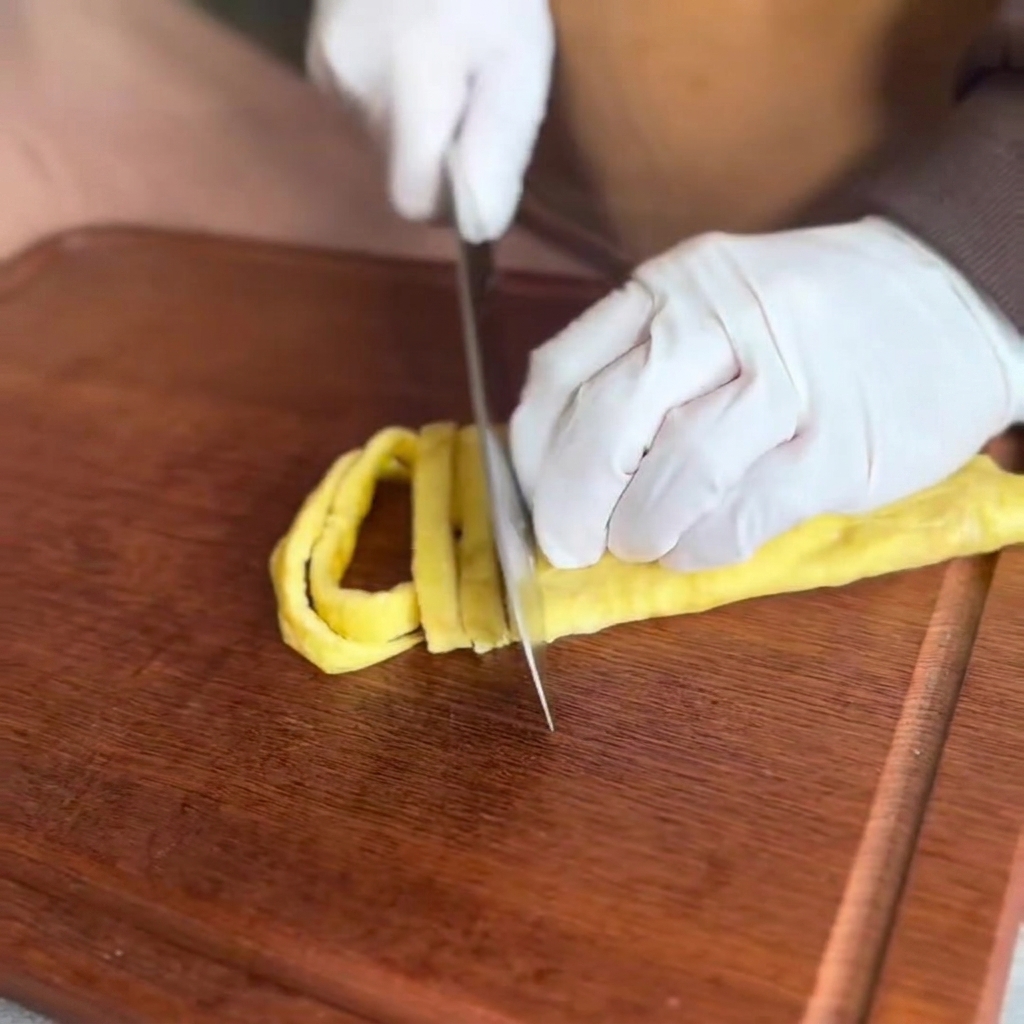 El panqueque de huevo cocido siendo cortado en tiras finas sobre una tabla de cortar de madera.
