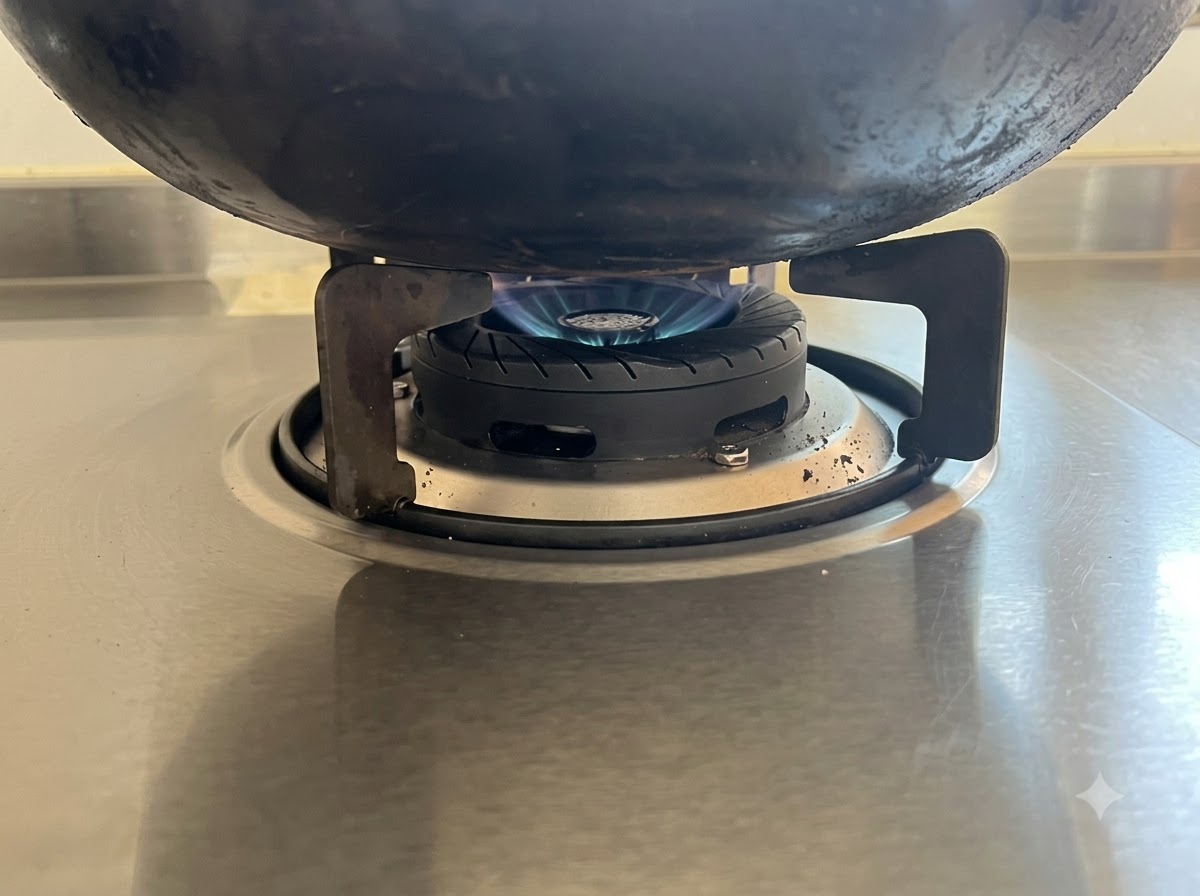 Una llama azul baja calentando la parte inferior de un wok negro en una estufa de acero inoxidable.