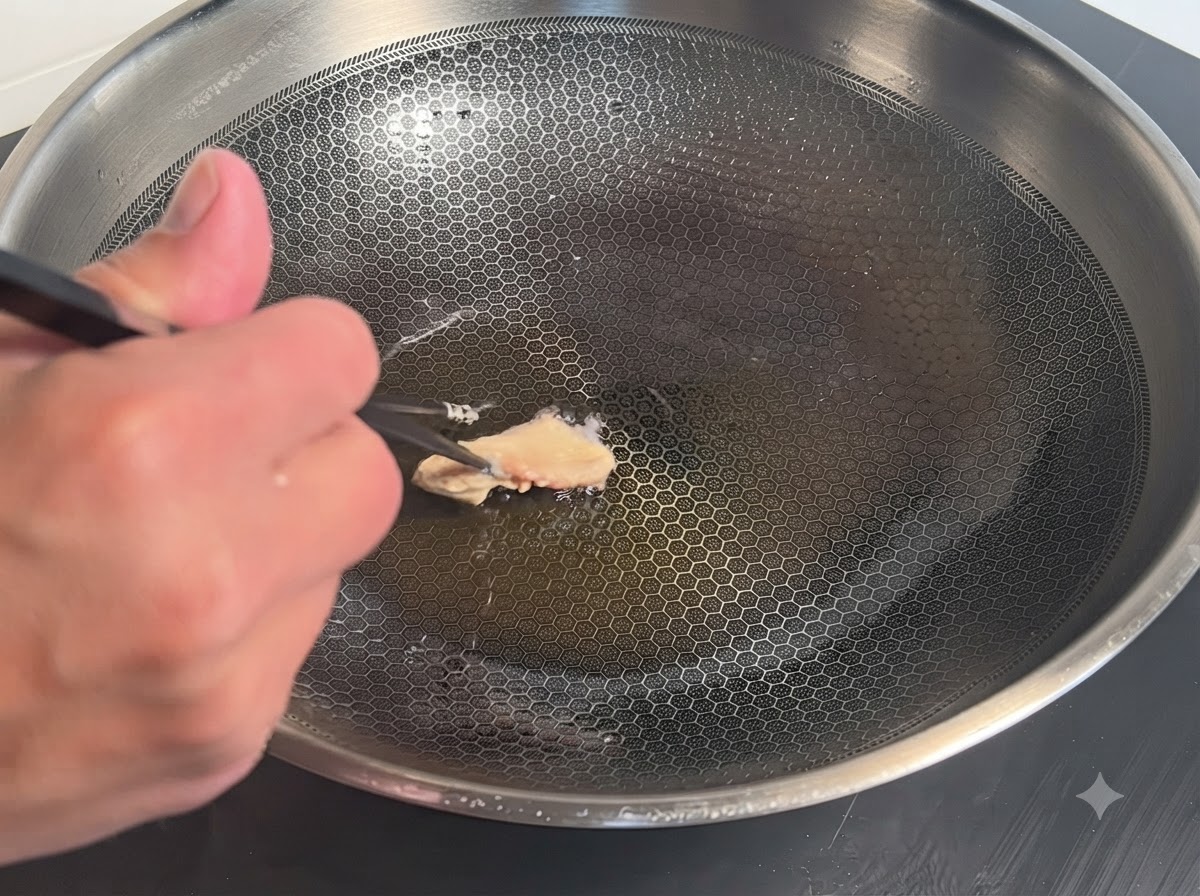 Una pieza de pollo rebozada colocada con palillos en un wok caliente con aceite.