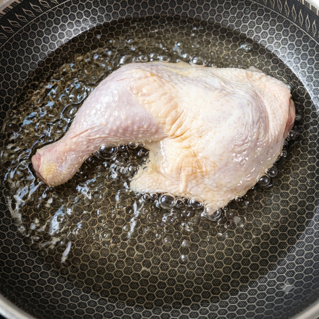 Un gran muslo de pollo crudo colocado dentro de una sartén llena de agua fría comenzando a calentar.