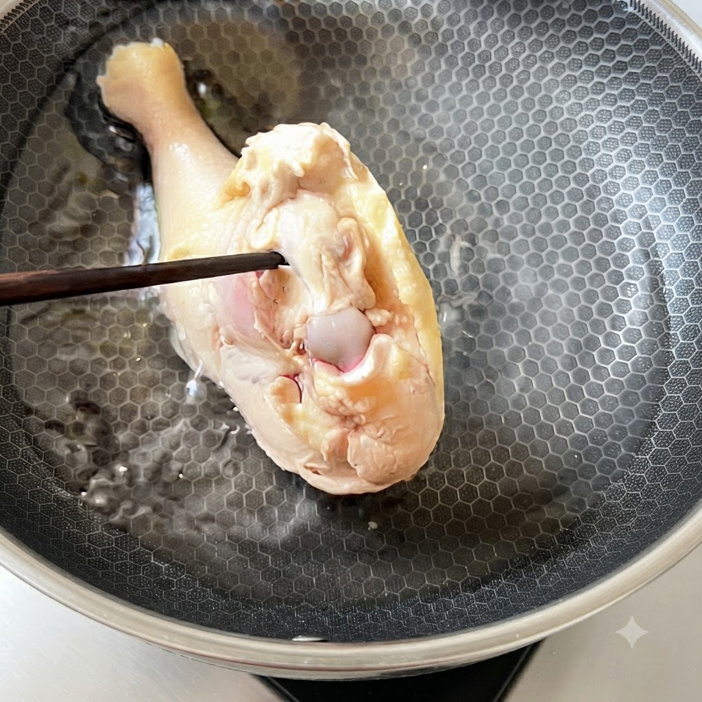 Un muslo de pollo escaldado siendo colocado nuevamente en agua fría dentro de una sartén de cocina.