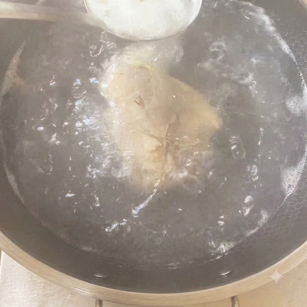 Una cuchara con condimento siendo añadida a una olla hirviendo que contiene el pollo y los aromáticos.