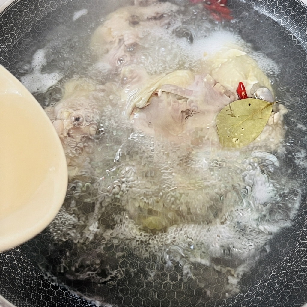 Una olla llena de caldo de pollo hirviendo, especias y una hoja de laurel cociéndose a fuego lento bajo calor.