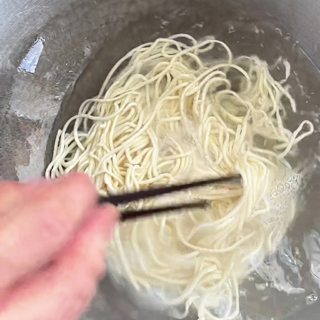 Fideos cocinándose en una olla siendo revueltos con palillos.