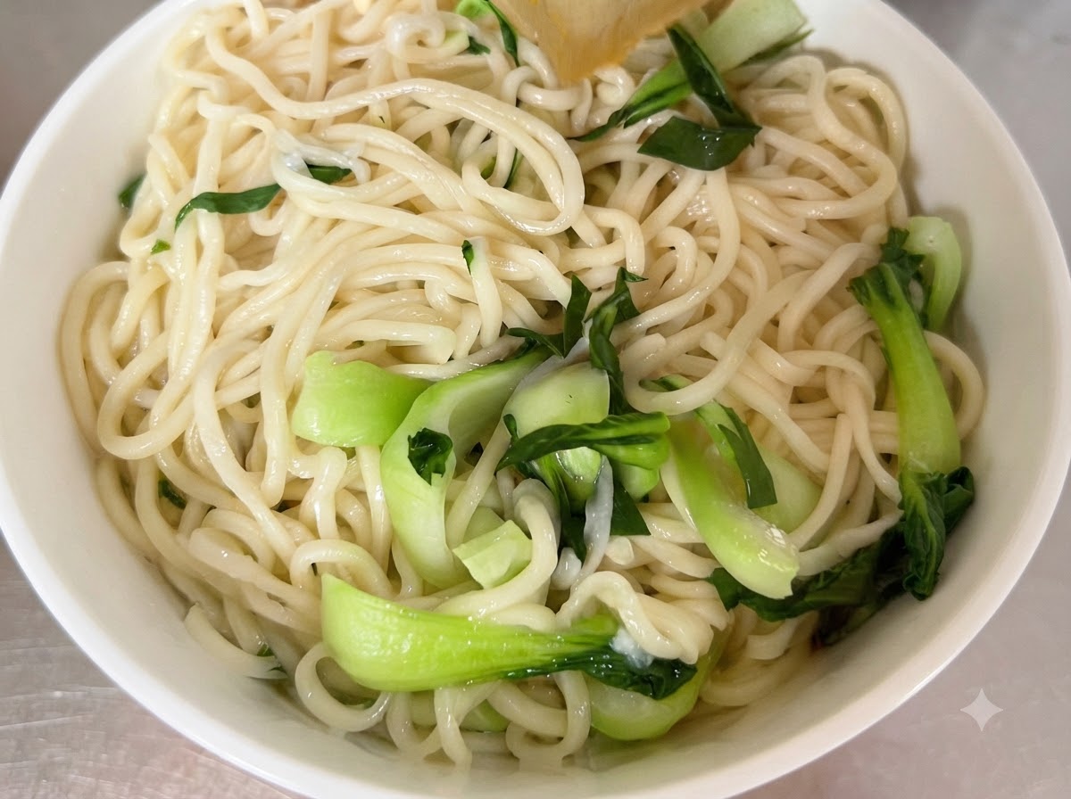 Fideos cocidos y bok choy fresco dispuestos dentro de un tazón blanco para servir.