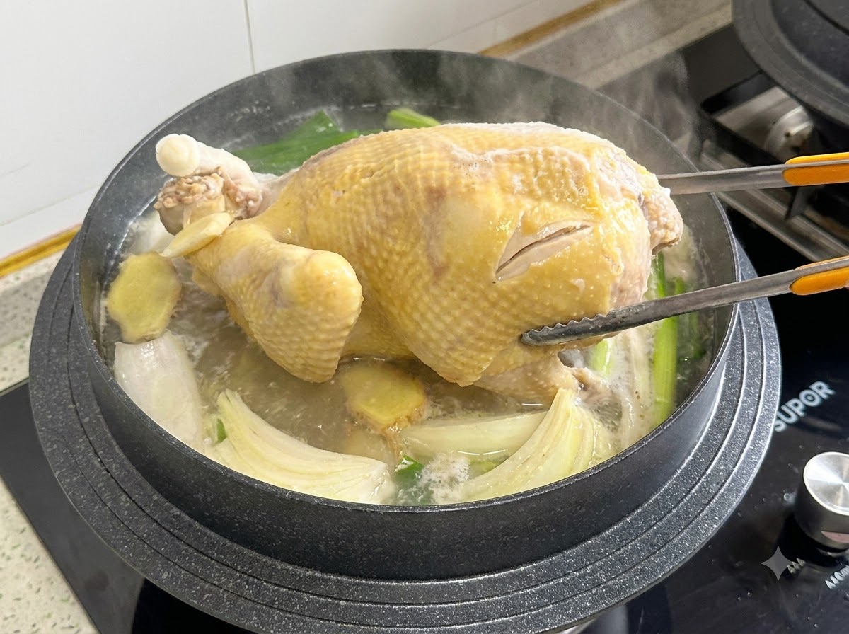 Pinzas de cocina sujetando y dando la vuelta a un pollo entero dentro de una olla de caldo hirviendo.