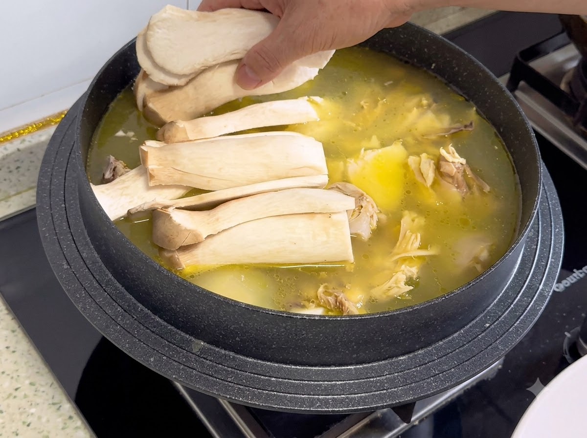 Setas de cardo en rodajas siendo colocadas encima del caldo de pollo y los ingredientes en una olla.