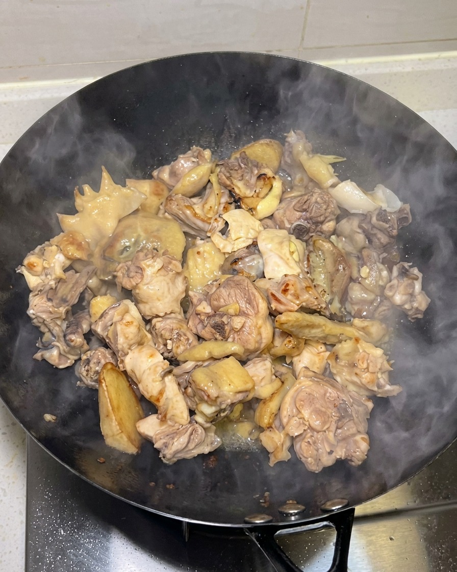 Trozos de pollo dorados cocinándose en un wok con vapor elevándose.