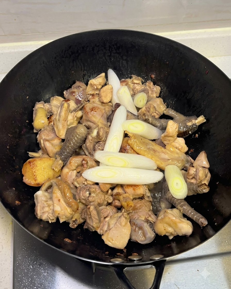 Añadiendo cebollines, ajo y especias enteras al wok con el pollo.
