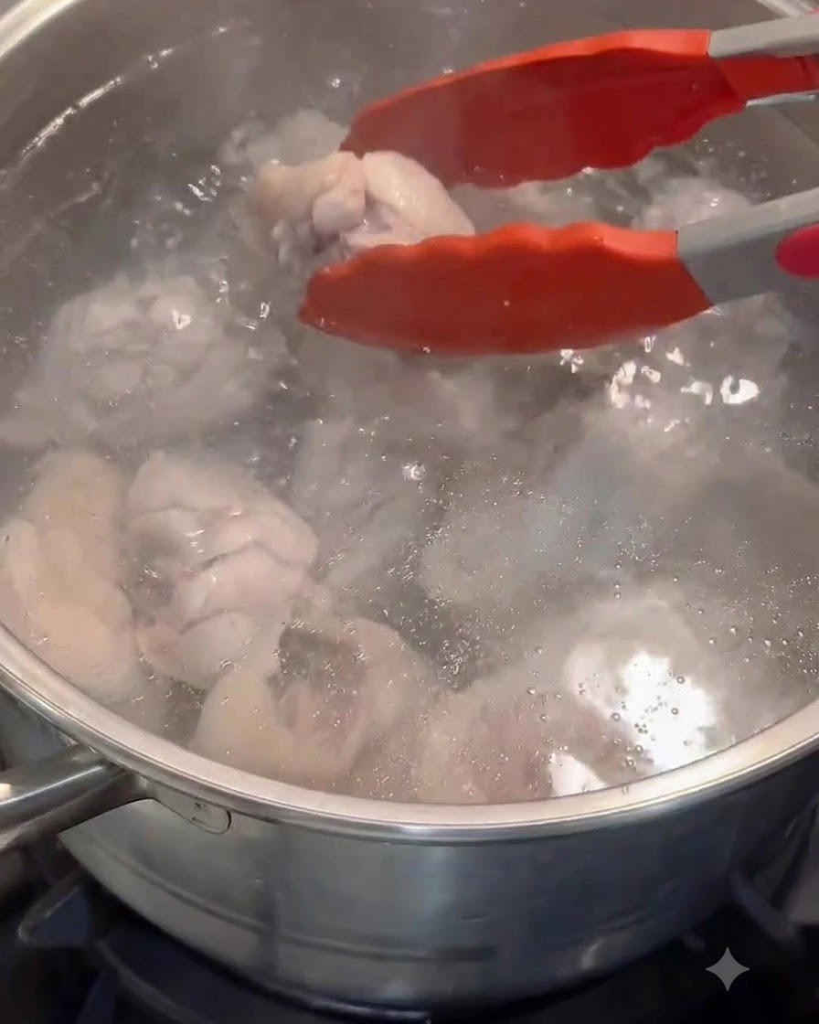 Pinzas rojas transfiriendo trozos de pollo blanqueados a una olla con agua caliente limpia.