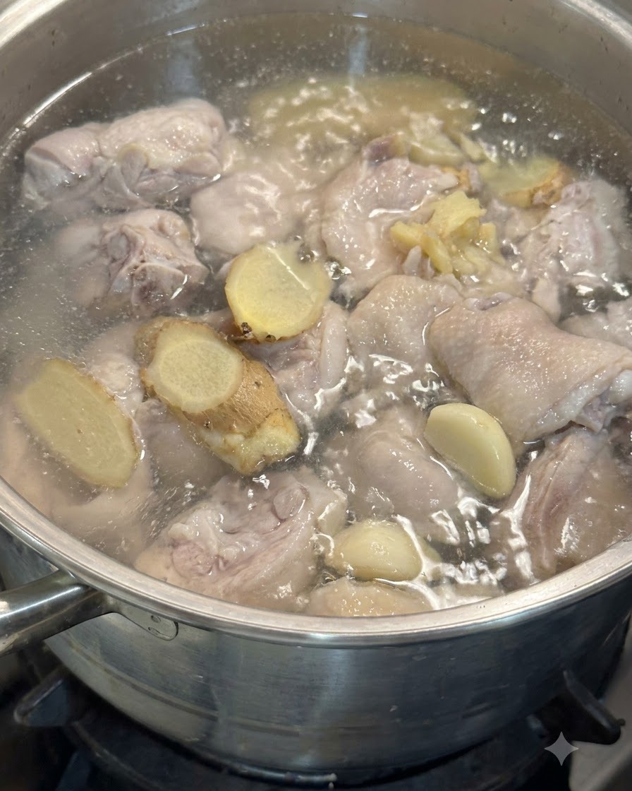 Dientes de ajo y rodajas de jengibre flotando en la olla con trozos de pollo en agua a fuego lento.