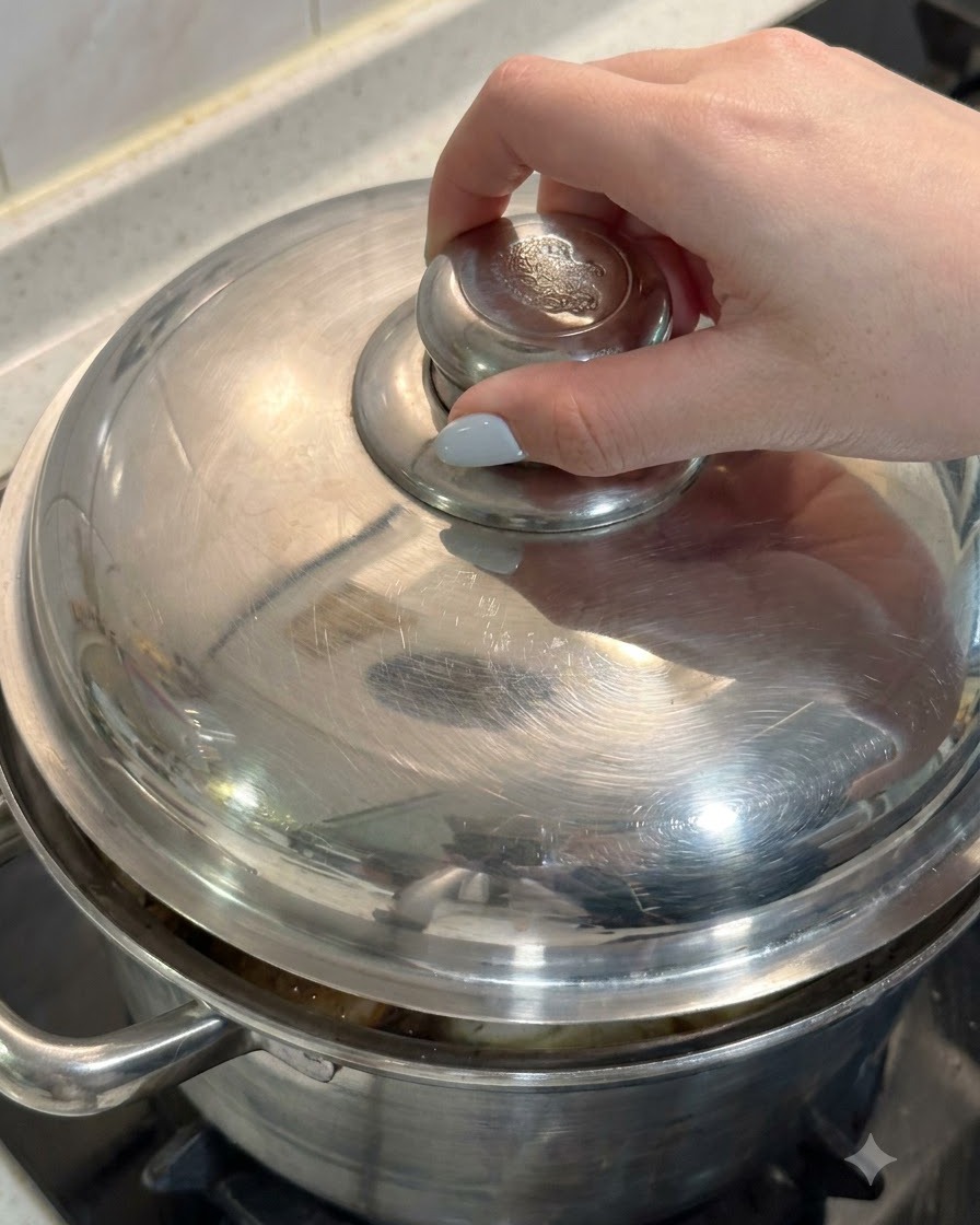 Una mano colocando la tapa de metal en una olla llena de pollo e ingredientes de sopa.