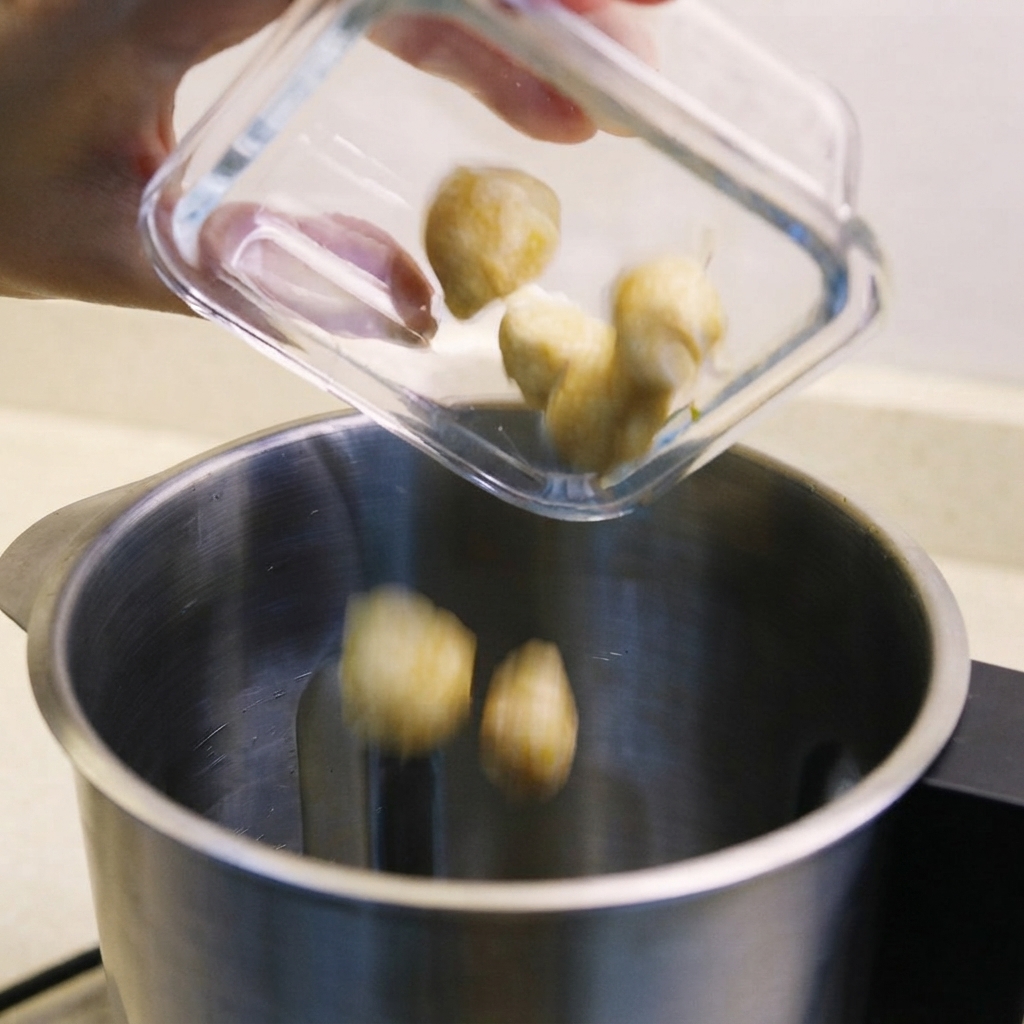 Nueces de candlenut, chalotas y belacan salteado siendo vertidos en el vaso de una licuadora.
