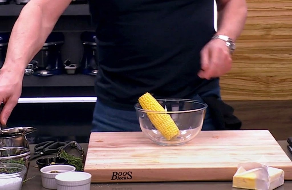Una mazorca de maíz cruda en un bol de vidrio, lista para ser sazonada con aceite de oliva, sal y pimienta.