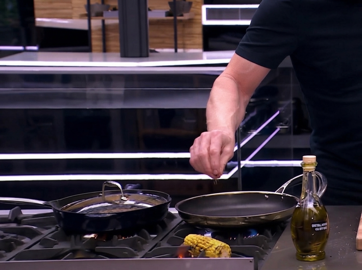 Una mazorca de maíz sazonada siendo asada y tostada directamente sobre una llama de gas abierta en la cocina.