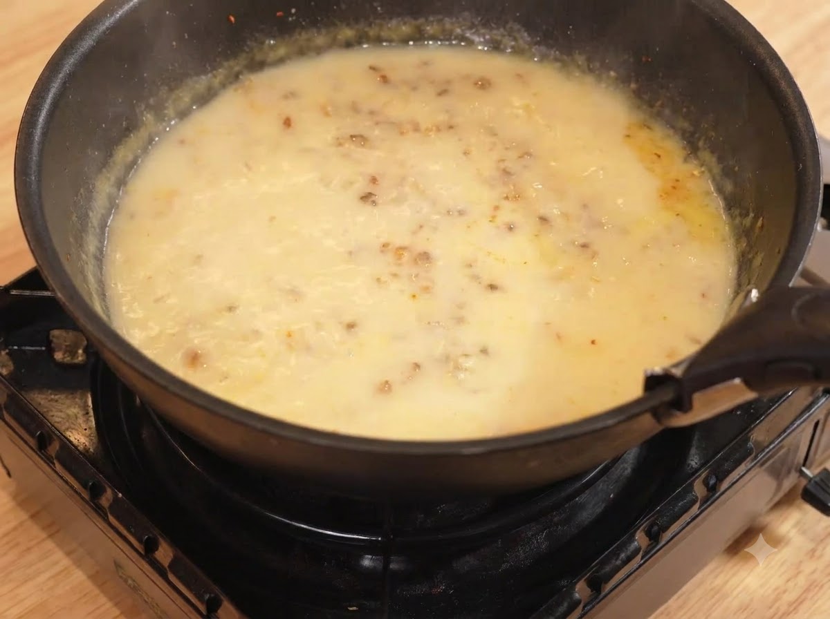 Agua y leche vertiéndose en la sartén con la mezcla de curry, cociendo a fuego lento.