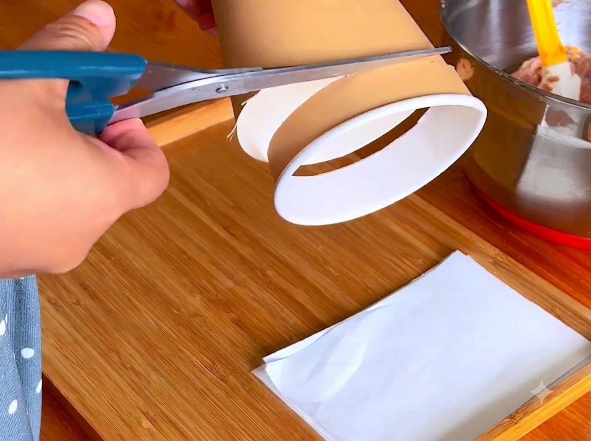 Un par de tijeras azules cortando el borde inferior de un vaso de papel en una tabla de madera.