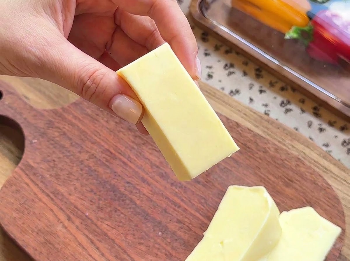 Primer plano de una mano sosteniendo un bloque rectangular de queso mozzarella preparado para rellenar.