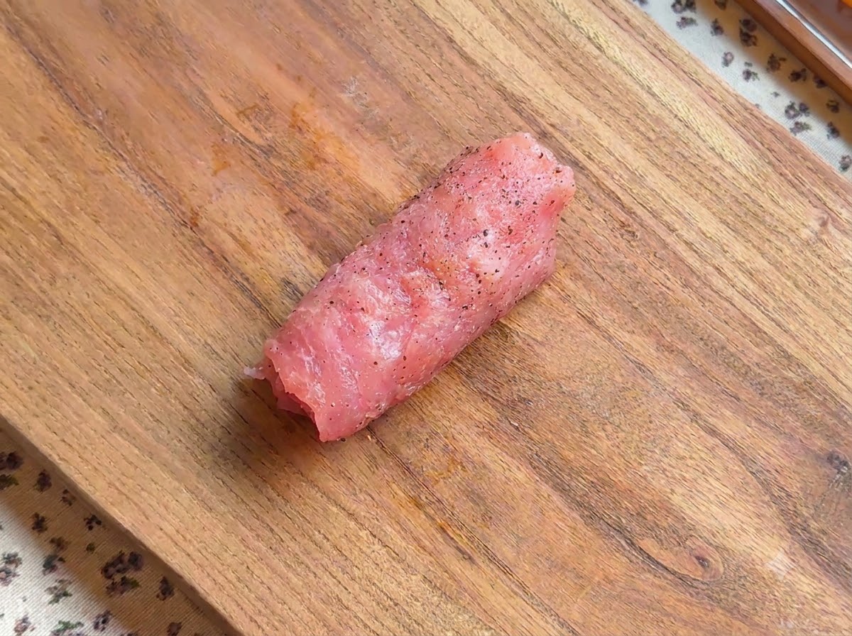 Un rollo de chuleta de cerdo sazonada reposando sobre una tabla de madera.