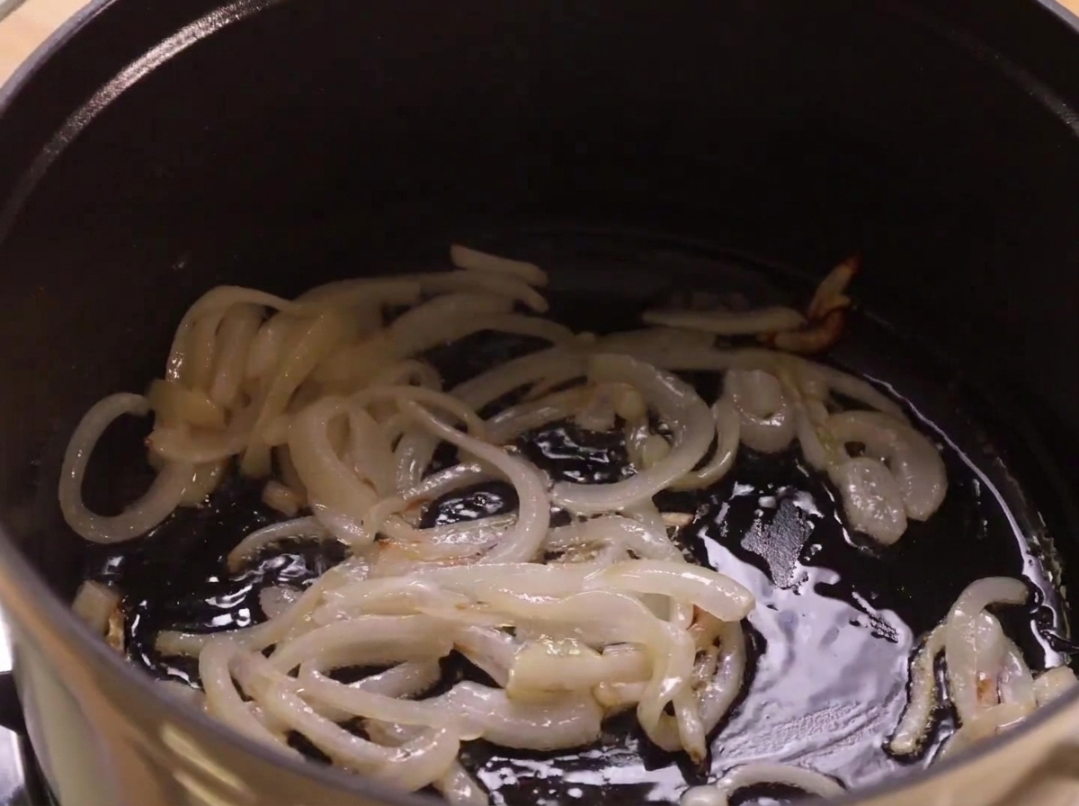 Cebollas salteándose en aceite en el fondo de una olla de cocina oscura.