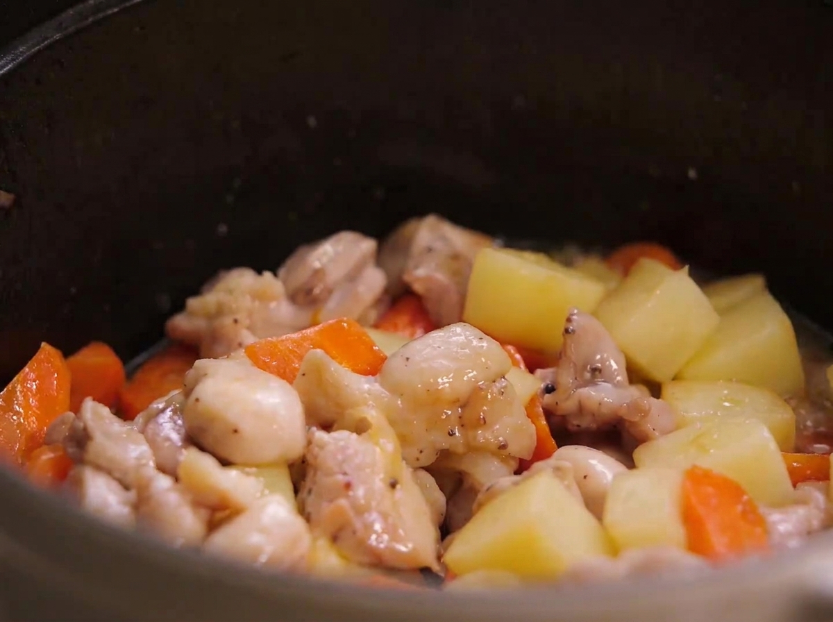Trozos de pollo frito, trozos de patata y trozos de zanahoria mezclados juntos dentro de una olla de guiso.