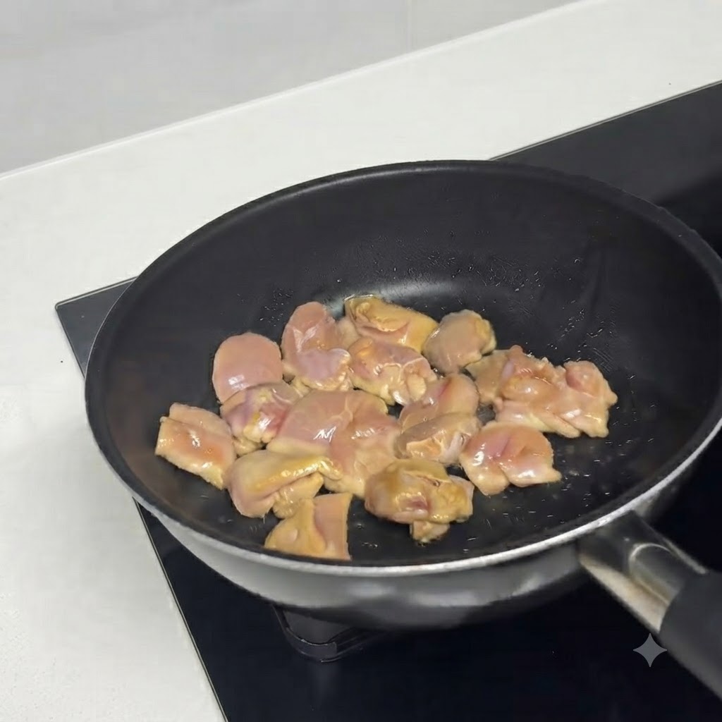 Trozos de pollo marinado chisporroteando en una sartén caliente con aceite.