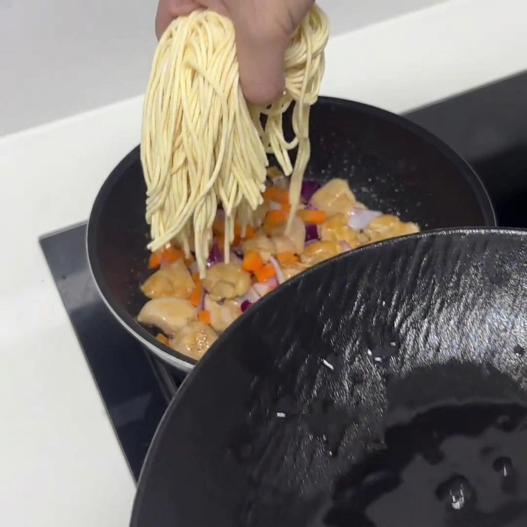 Fideos de pasta remojados previamente siendo añadidos a la sartén con el pollo y las verduras.