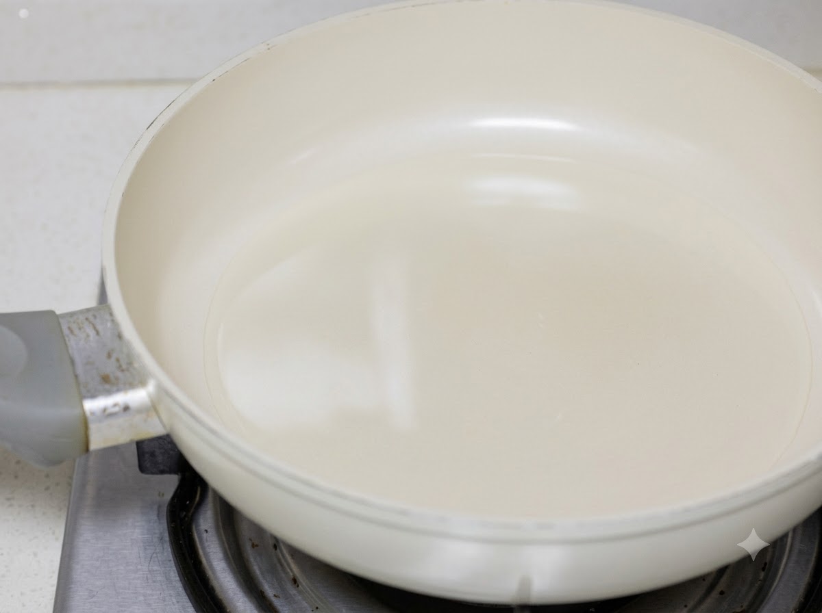 Trozos de pollo friéndose en aceite de cocina dentro de una sartén blanca.
