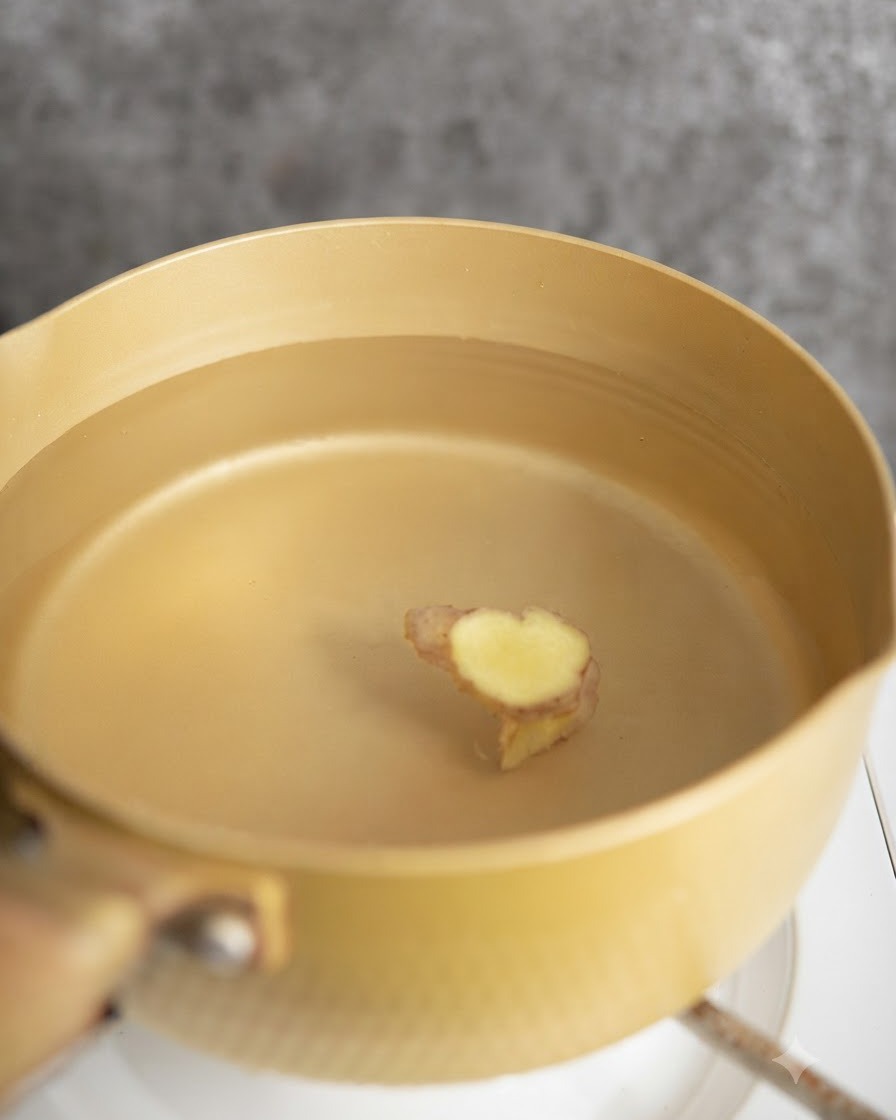 Trozos de pollo escaldándose en una olla con agua y rodajas de jengibre.