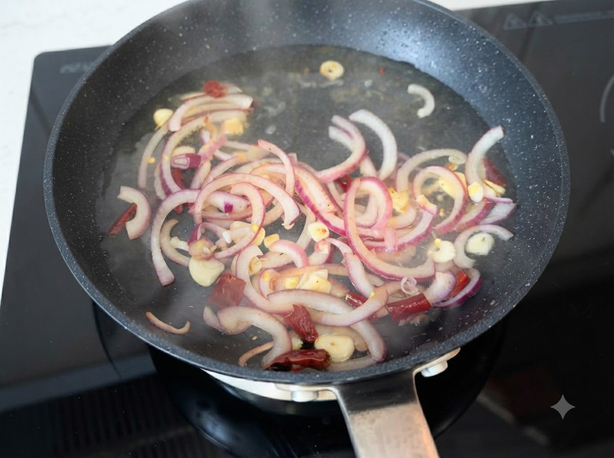 Agua caliente siendo vertida sobre rodajas de cebolla morada, ajo y chiles salteados en una sartén.
