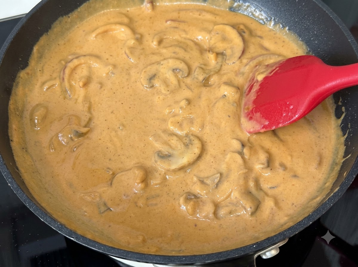 Rodajas de champiñones mezcladas en salsa de crema de curry a fuego lento en una sartén.