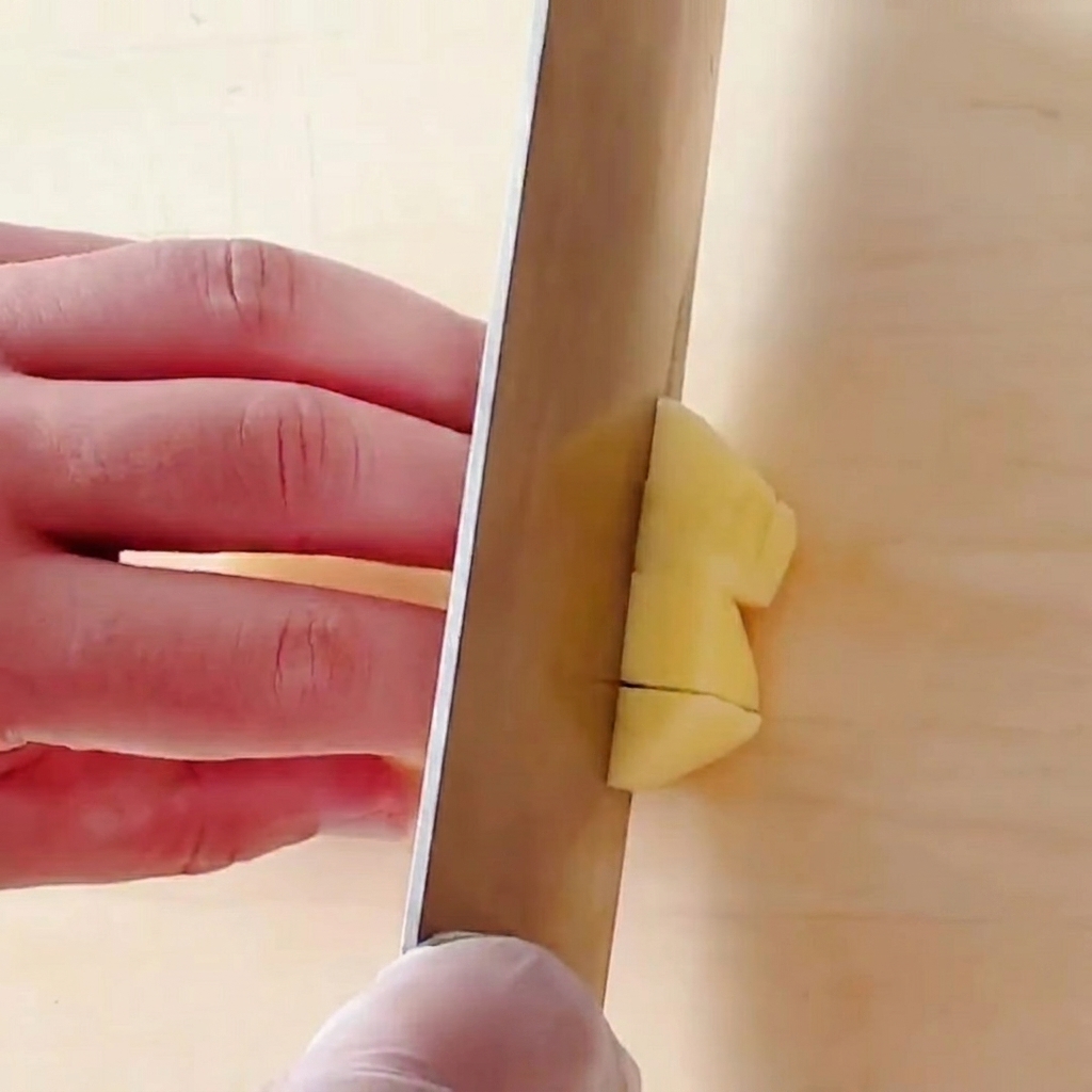 Patatas cortadas en pequeños cubos cuadrados sobre una tabla de cortar de madera.