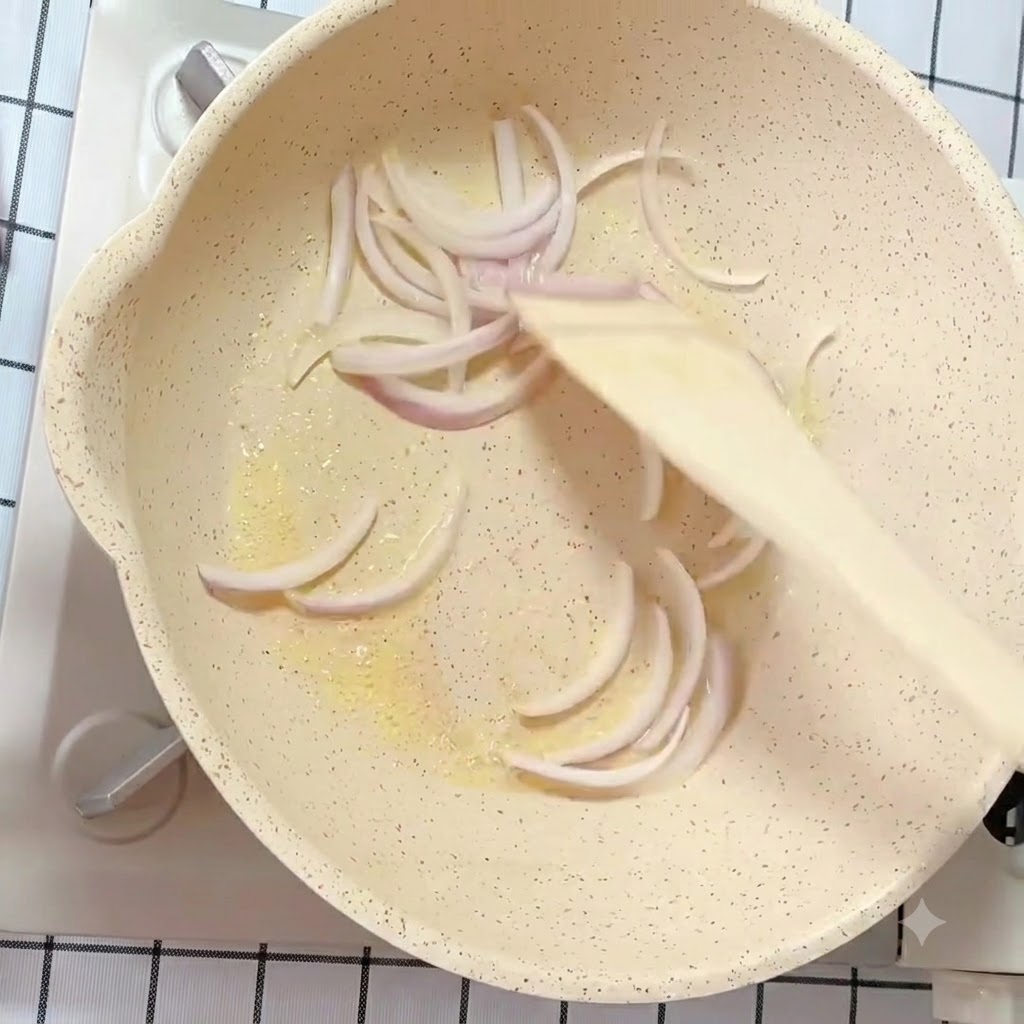 Tiras de cebolla blanca y morada salteándose en una sartén con mantequilla y una espátula de madera.