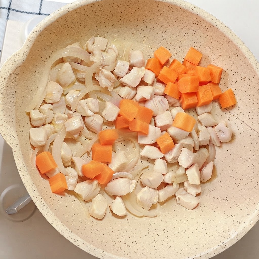 Cubos de zanahoria de color naranja brillante añadidos a la sartén que contiene pollo y cebollas.
