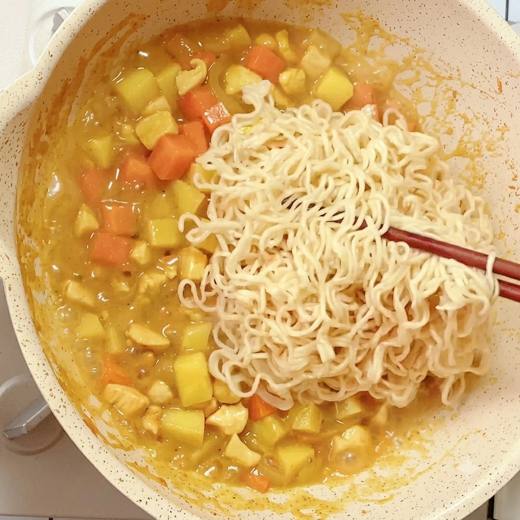 Fideos instantáneos precocidos colocados con palillos en una sartén con la mezcla de curry reduciéndose.