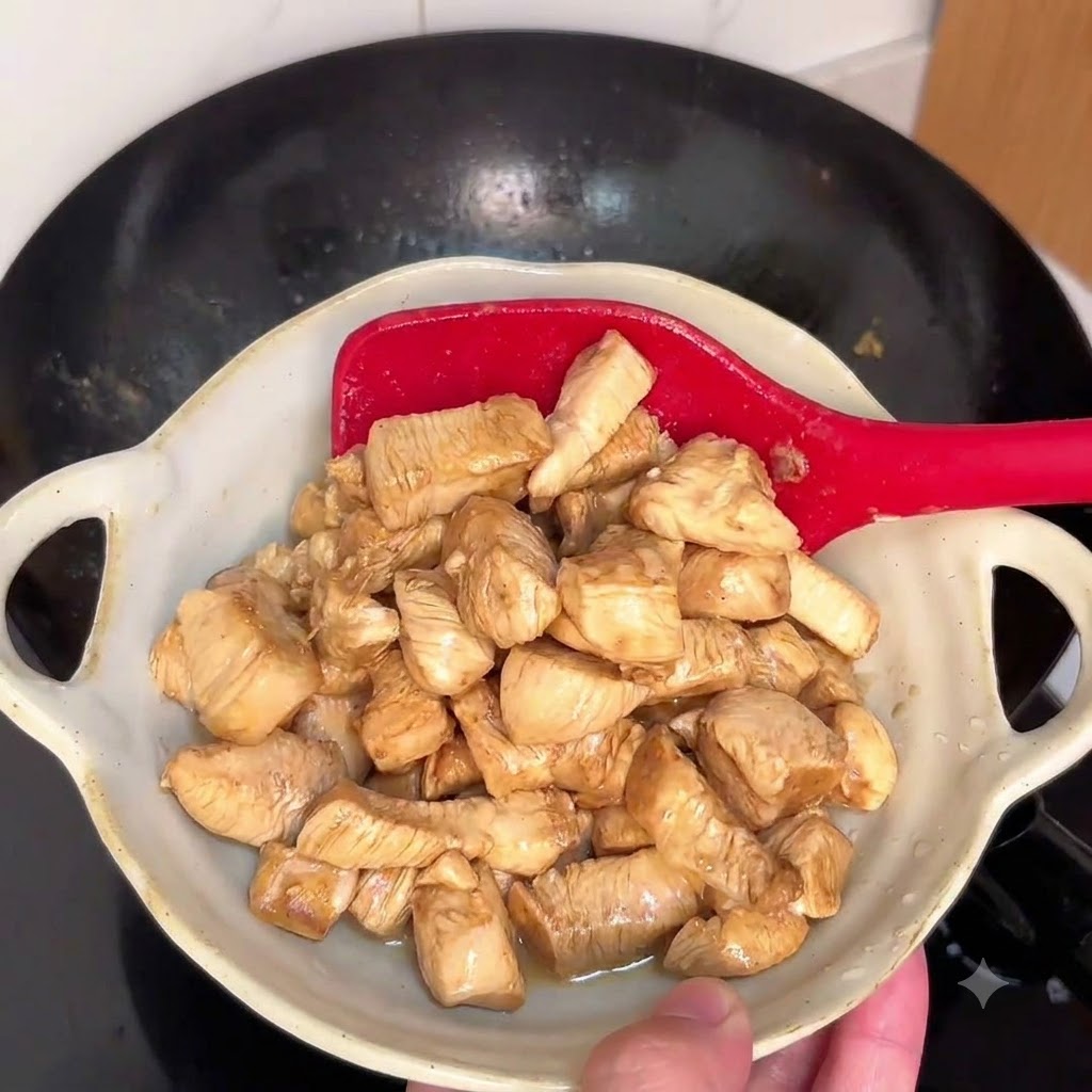 Trozos de pollo salteándose en un wok caliente con una espátula roja.