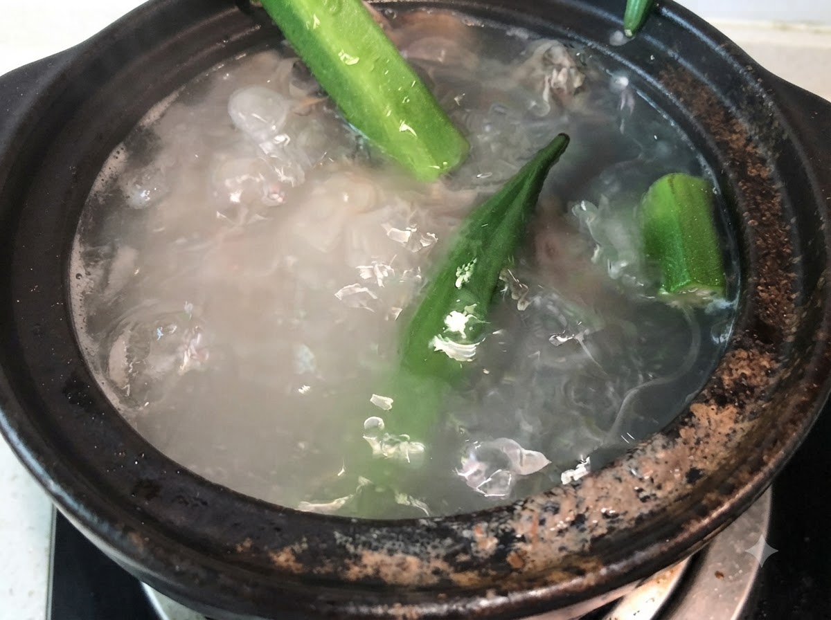 Vainas de okra verde entera agregándose al caldo hirviendo de huesos de cerdo.