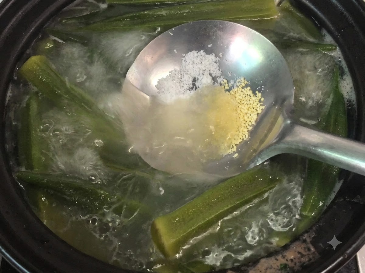 Un cucharón sosteniendo sal y polvo de pollo sobre una olla humeante de sopa de okra y huesos.