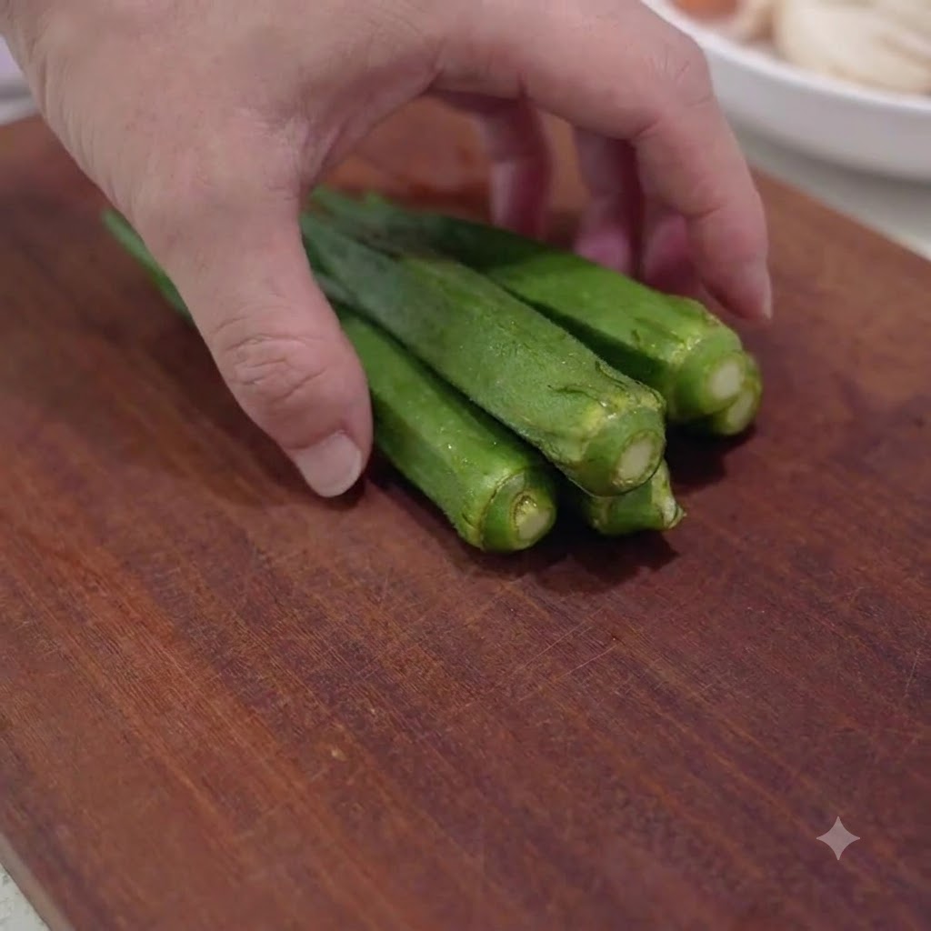 Vainas de okra verde fresca cortadas en rodajas pequeñas sobre una tabla de cortar de madera.