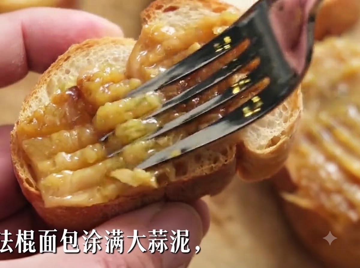 Un tenedor untando pasta gruesa de ajo asado sobre una rebanada de baguette crujiente.
