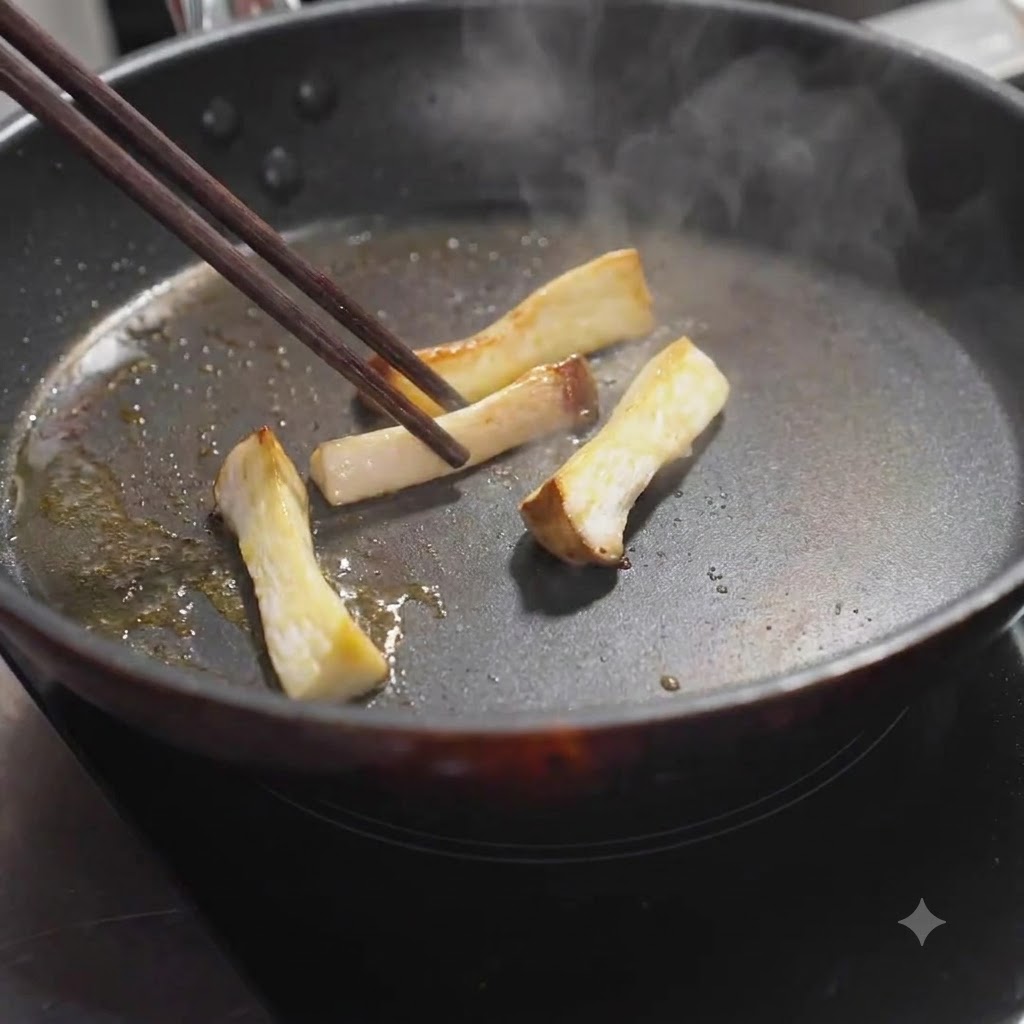 Rodajas de champiñones ostra rey siendo volteadas en la sartén con palillos hasta dorarse.