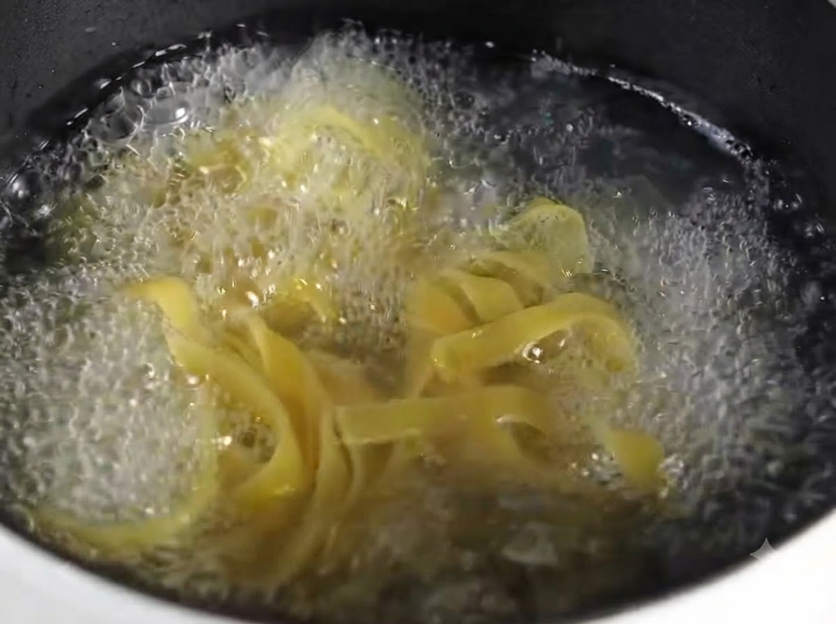 Una vista cercana de pasta fettuccine cocida amontonada ordenadamente en un plato redondo gris.