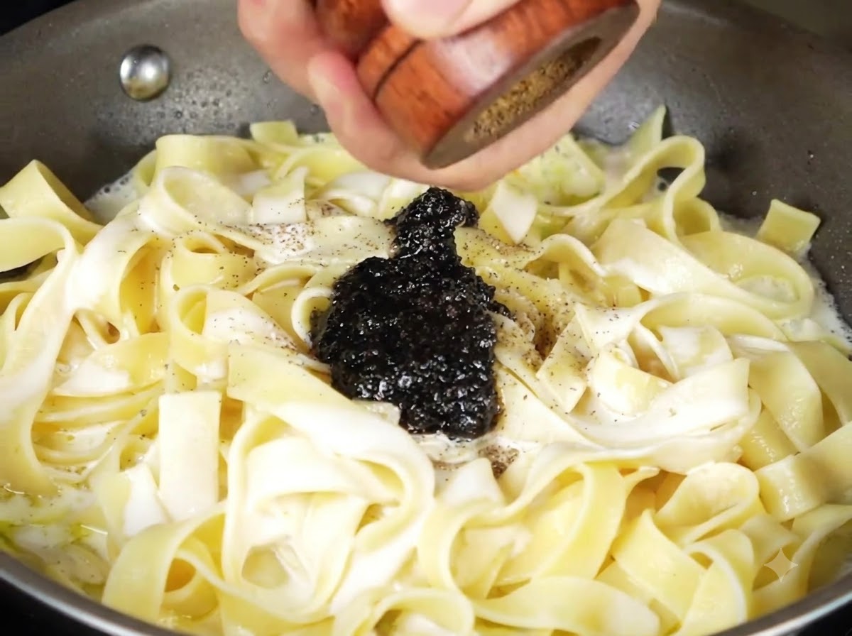 Salsa de trufa negra y pimienta negra recién molida encima de la pasta cremosa en la sartén.
