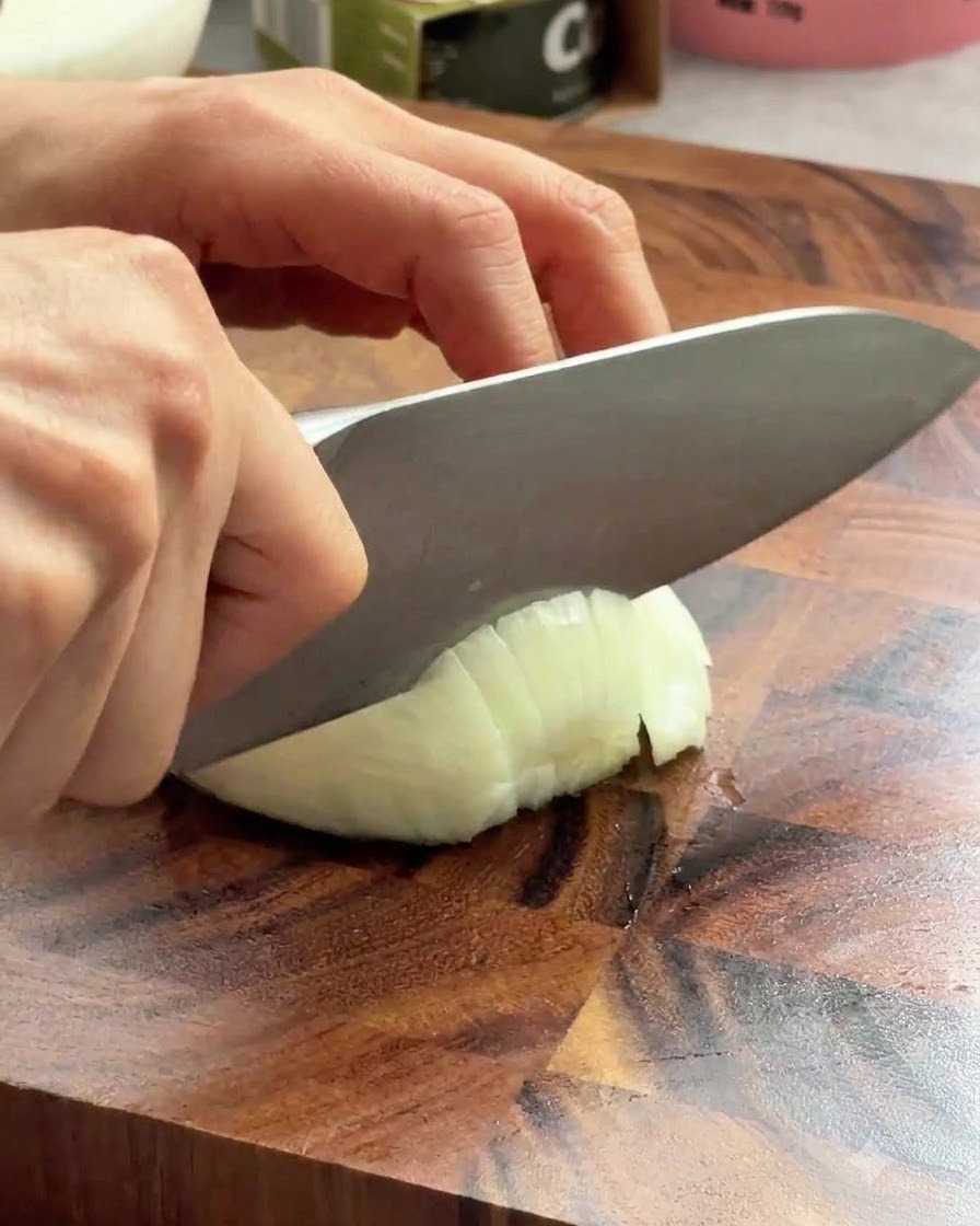 Un cuchillo de chef afilado rebanando una cebolla blanca en una tabla de madera.